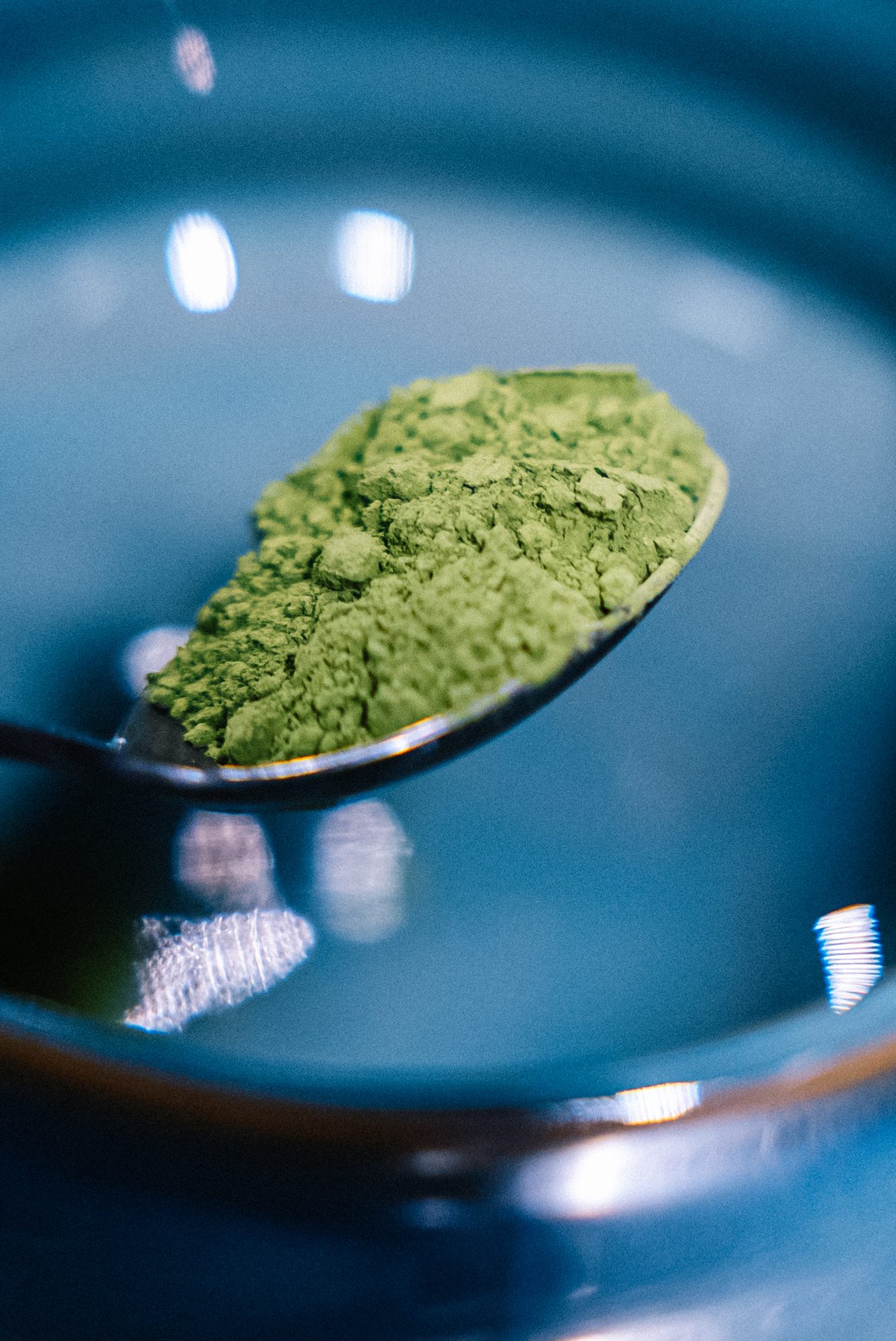 Matcha powder on a spoon over a dark ceramic bowl.