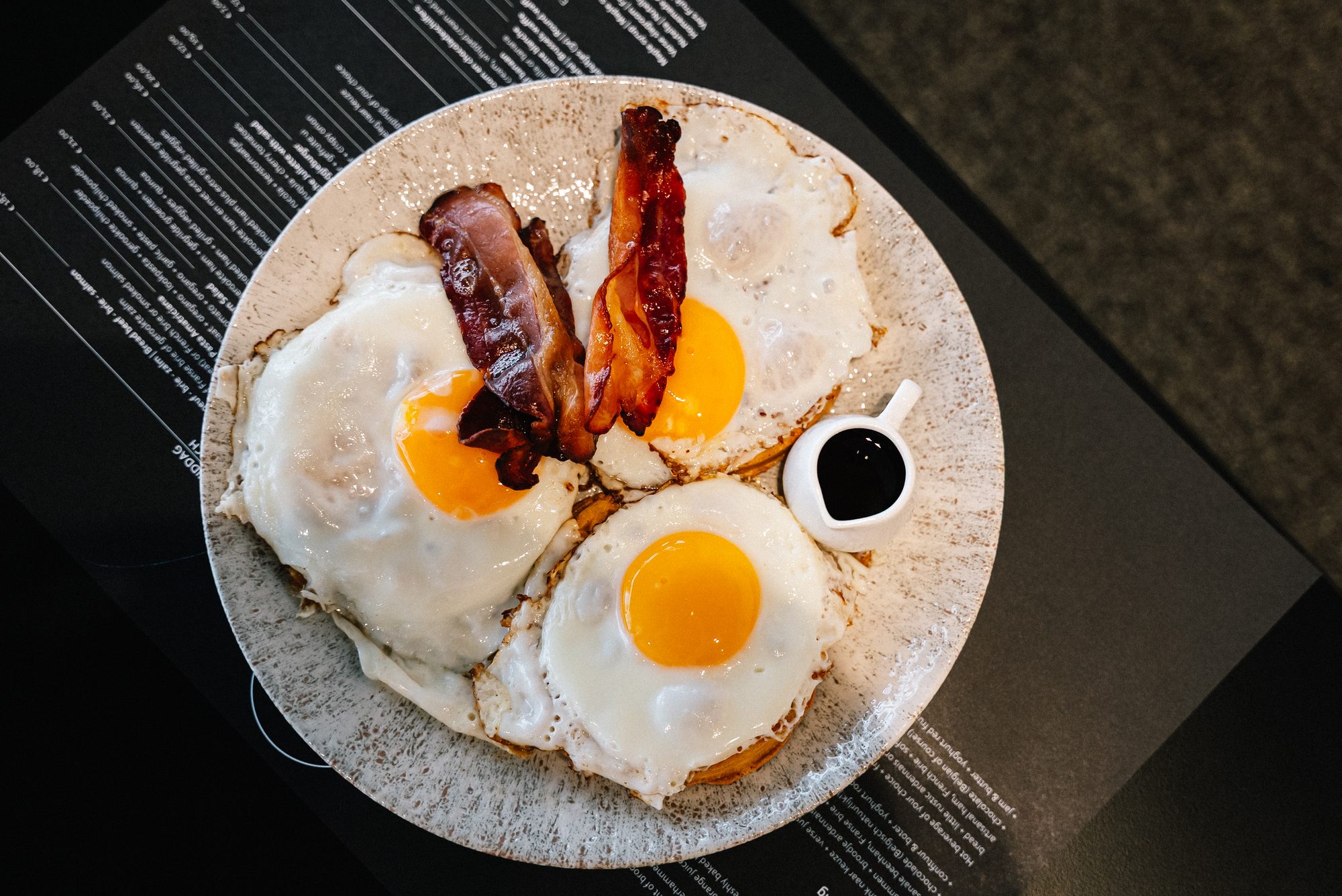 Fried eggs & crispy bacon over the black menu.
